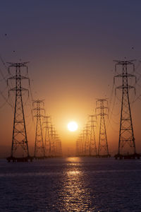 Silhouette electricity pylon by sea against romantic sky at sunset