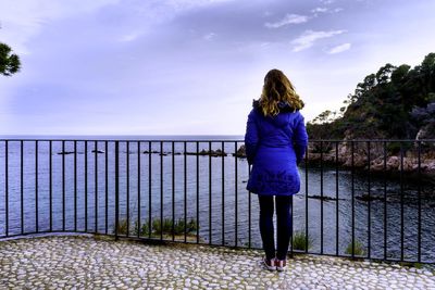 Rear view of woman standing on railing against sky