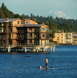Man paddleboarding on lake with buildings in background