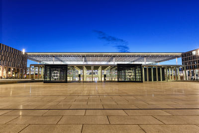 Empty footpath by buildings against blue sky