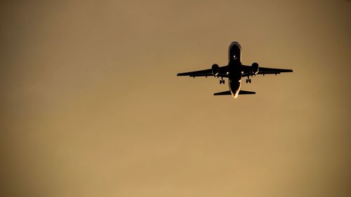 Low angle view of silhouette airplane flying against clear sky during sunset