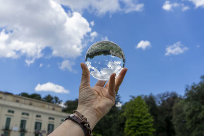 Midsection of person holding crystal ball against sky