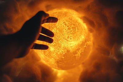 Close-up of hand holding light painting against orange sky