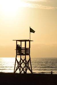 Lifeguard hut on beach against sky during sunset