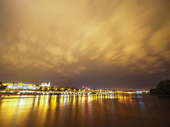 Illuminated buildings by sea against sky during sunset