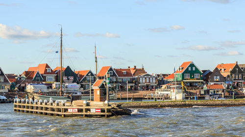 Sailboats in sea by buildings against sky