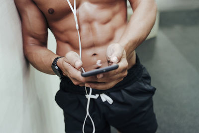 Mid adult sportsman using mobile phone while leaning on wall at gym