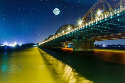 Illuminated bridge over river against sky at night