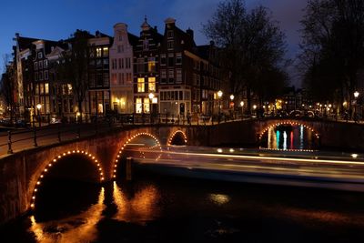 Blurred motion of ferry sailing towards arch bridge over canal at night