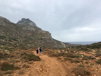 Rear view of hikers walking on landscape towards mountain
