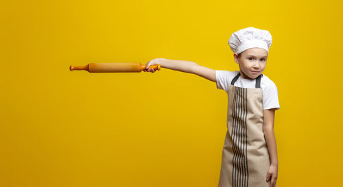 Portrait of young woman standing against yellow background