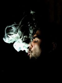 Close-up of young man smoking against black background