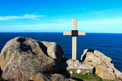 Close-up of cross on rock by sea against sky