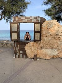 Portrait of smiling woman looking through window against sea