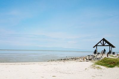 People sitting in gazebo at beach against sky