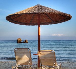 Deck chairs by sea against sky