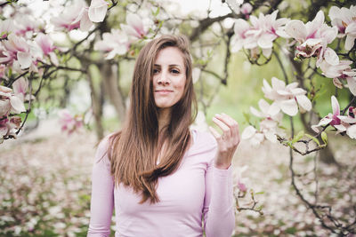 Cheerful long hair young woman under the blooming magnolia. spring park