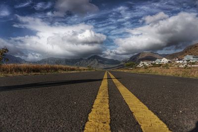 Empty road by mountains against cloudy sky