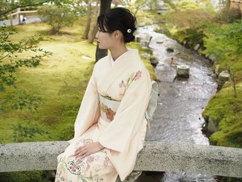 Woman in kimono sitting against canal