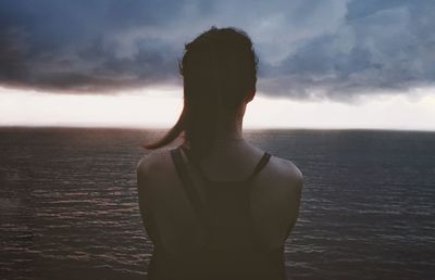 Rear view of woman standing by sea against sky