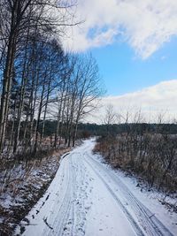 Tire tracks on snow covered road against sky