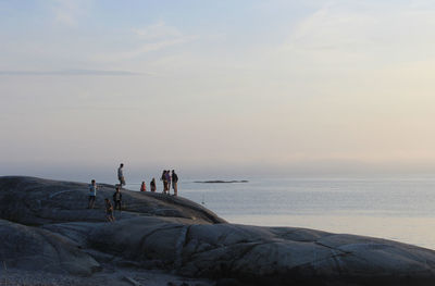 People on mountain by sea against sky during sunset