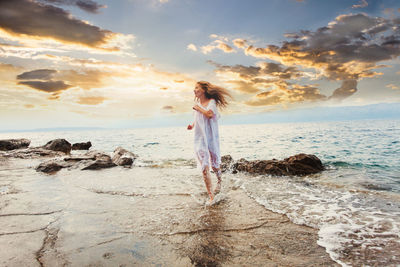 Man standing on rock by sea against sky during sunset