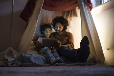 Father and daughter sitting in dark children's room, looking at digital tablet