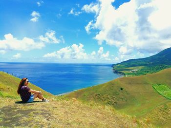 Woman sitting on shore by sea against sky