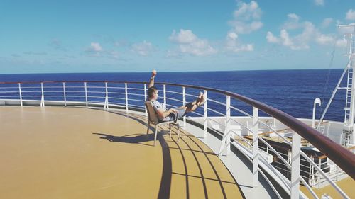 Side view of man with arms raised sitting on cruise ship sailing in sea