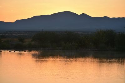 Scenic view of lake by silhouette mountains against orange sky