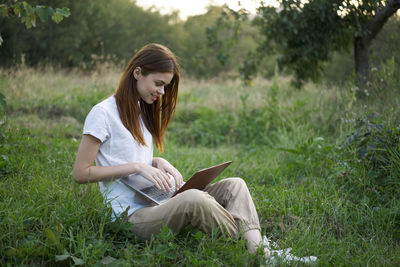 Young woman using laptop while sitting on field