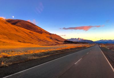 Empty country road along landscape and mountains against blue sky