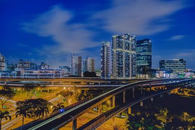 Illuminated bridge by buildings against sky in city