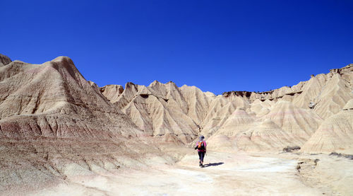 Man walking on rock formation against clear blue sky