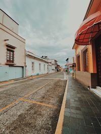 Empty road by buildings in city against sky