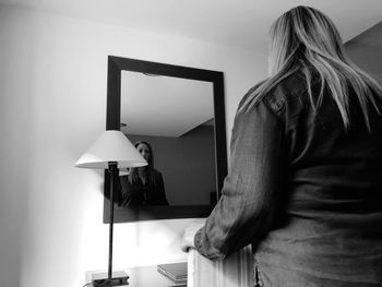 Rear view of woman standing against wall at home