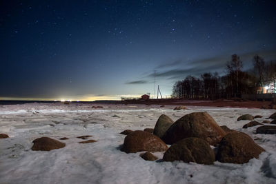 Scenic view of rocks amidst snow at beach against sky during night