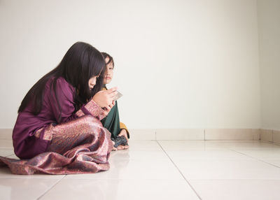 Siblings playing video game while sitting on floor at home