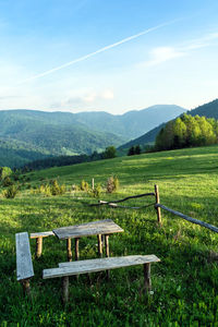 Scenic view of a wooden bench with table on a field against sky