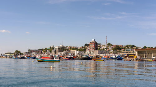 Boats moored in river by buildings against sky