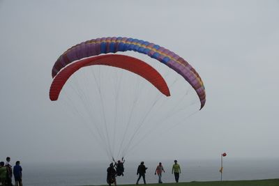Paragliders amidst people at beach against sky