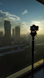 Silhouette of photographing on city street against sky during sunset