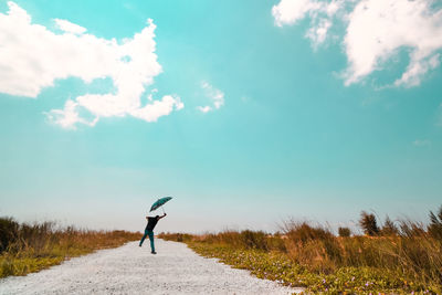 Man with umbrella levitating over road against sky