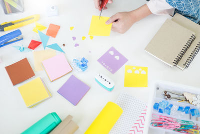 Midsection of woman cutting adhesive notes with various objects on table