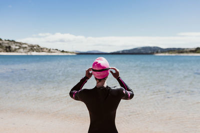 Rear view of woman wearing wetsuit standing at beach