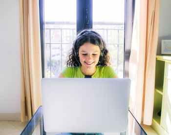 Portrait of smiling young woman using laptop on window