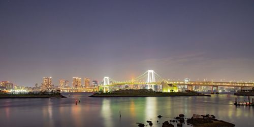 Illuminated bridge over river in city against sky at night