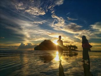 Silhouette people standing on beach against sky during sunset