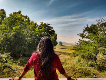 Rear view of woman walking on field against sky